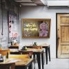 Super-Seat | Café interior | Wooden tables and chairs in natural tones, neon "MAGIC" sign in gold frame, wooden door at right. | Hospitality Furniture